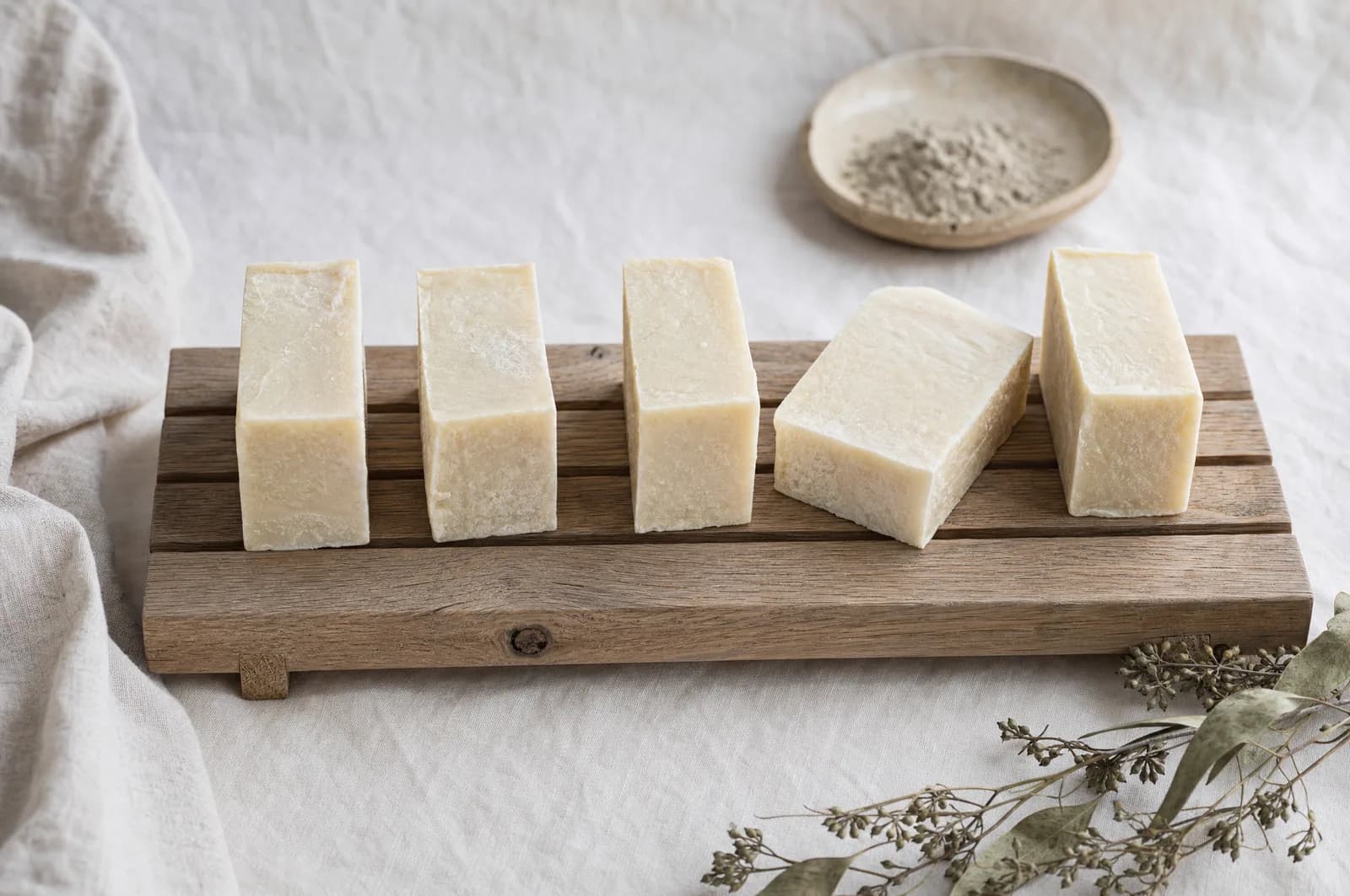 Hand-cut pale tallow soap bars curing on a wooden rack on soft linen.