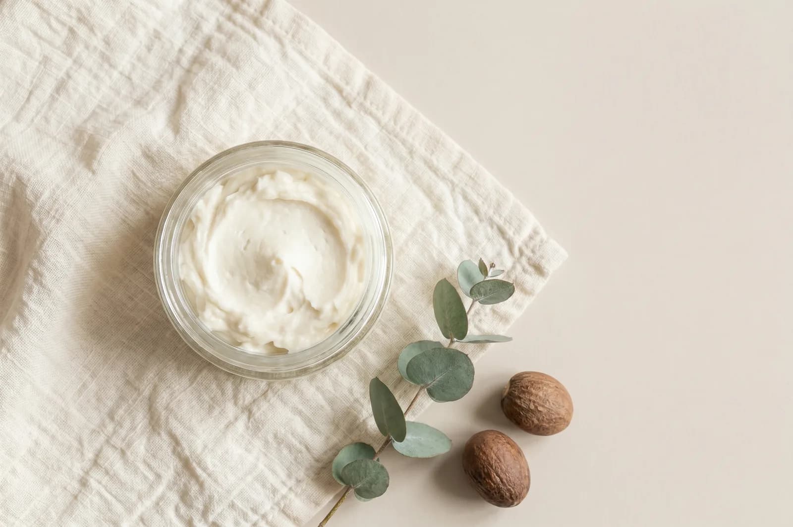 A jar of soft, whipped tallow and shea lotion on pale linen with a small sprig of greenery.