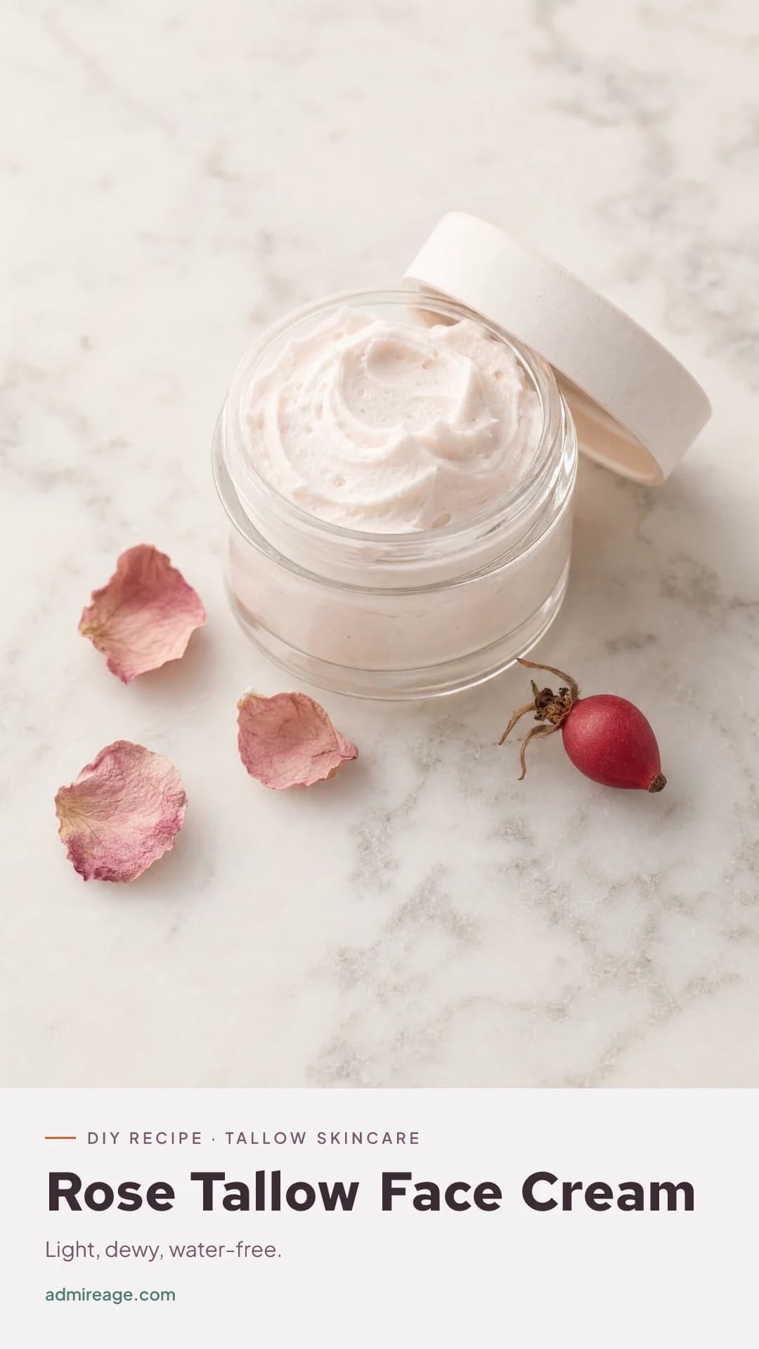 A jar of airy, rose-tinted whipped tallow face cream with rose petals on marble.