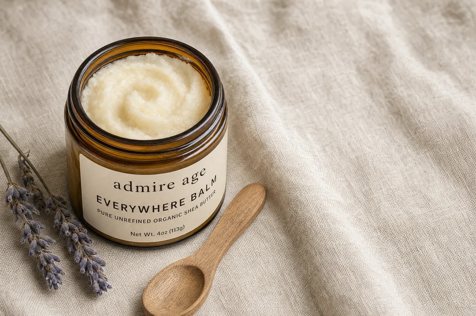 An open jar of softly whipped tallow balm with soft peaks on pale linen, beside dried lavender and a wooden spoon.