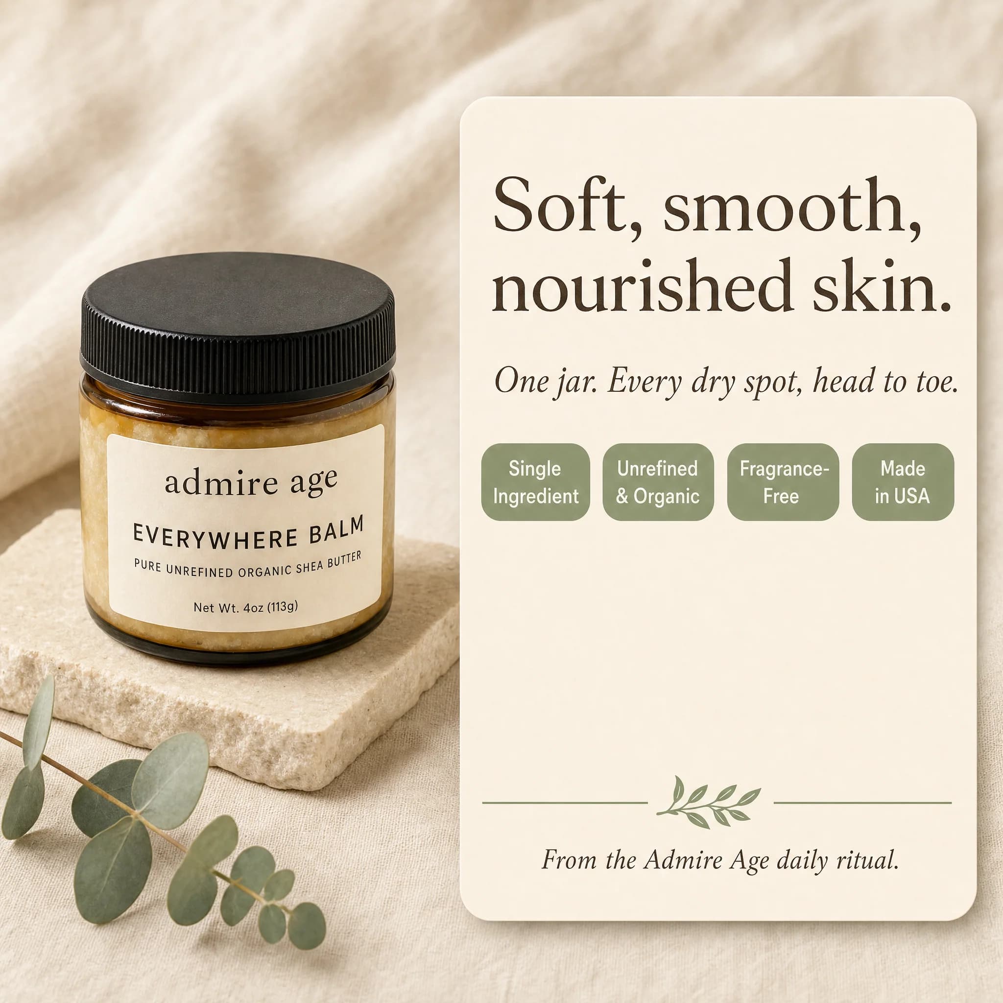 Admire Age Everywhere Balm amber glass jar on a pale stone riser with eucalyptus sprigs beside a card reading Soft, smooth, nourished skin — One jar. Every dry spot, head to toe.