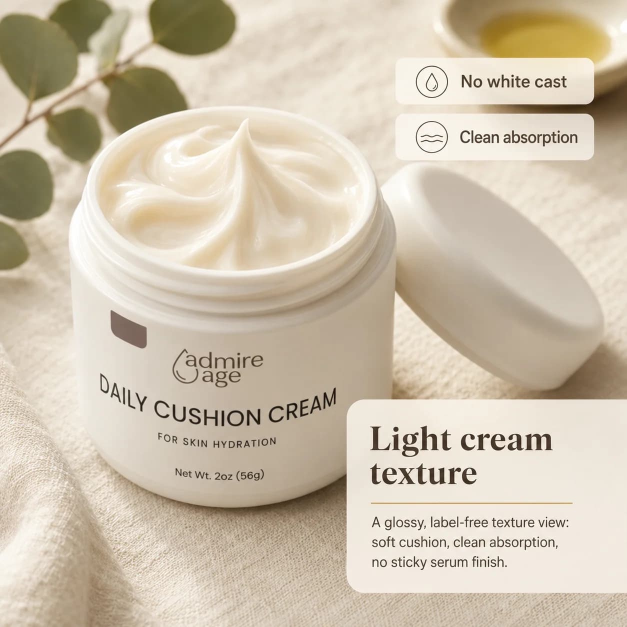 Open Daily Cushion Cream jar showing a soft, swirled white cream peak with the lid resting beside it on linen, eucalyptus stems and a small ceramic dish of oil in the background, and a card to the right titled 'Light cream texture' with No white cast and Clean absorption callouts