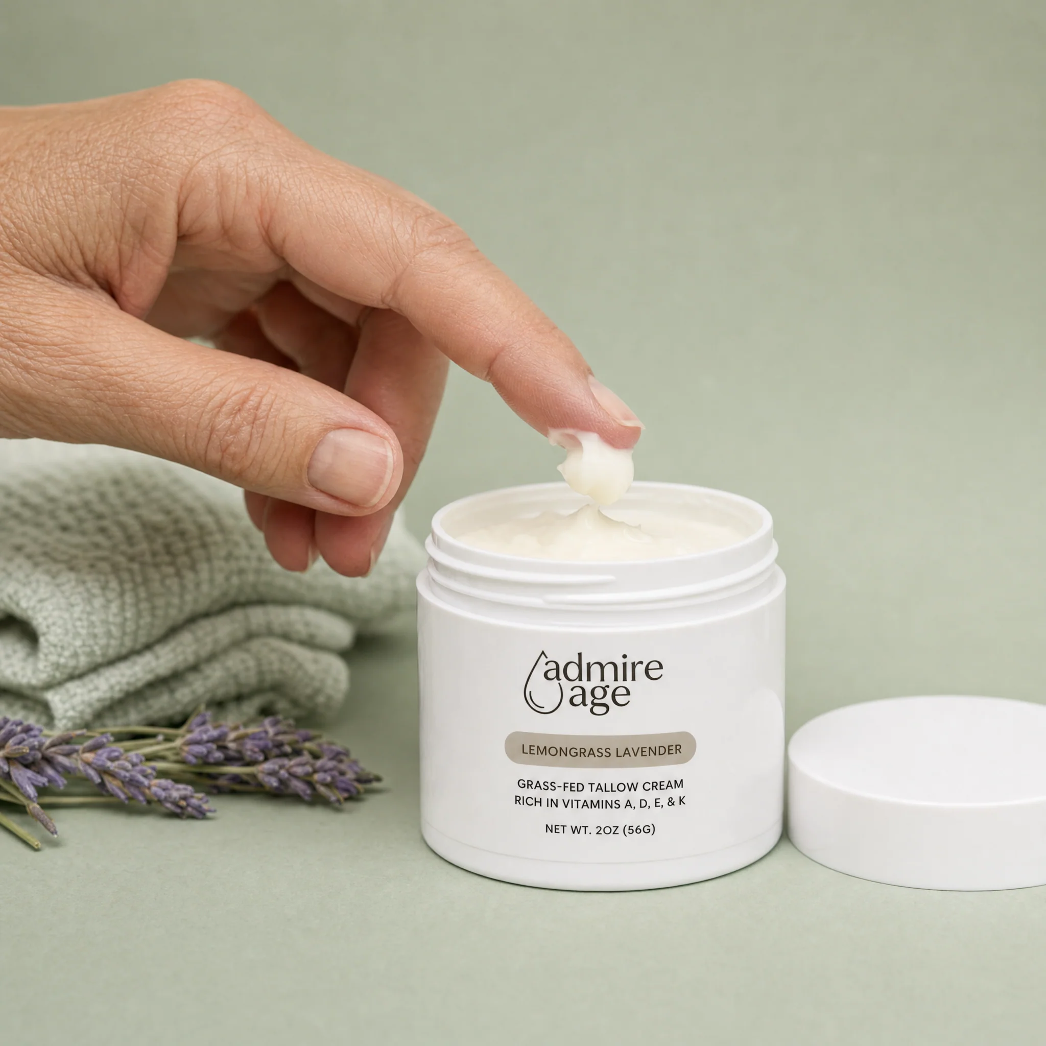 A hand lifting a small dollop of Lemongrass Lavender tallow cream from the open jar