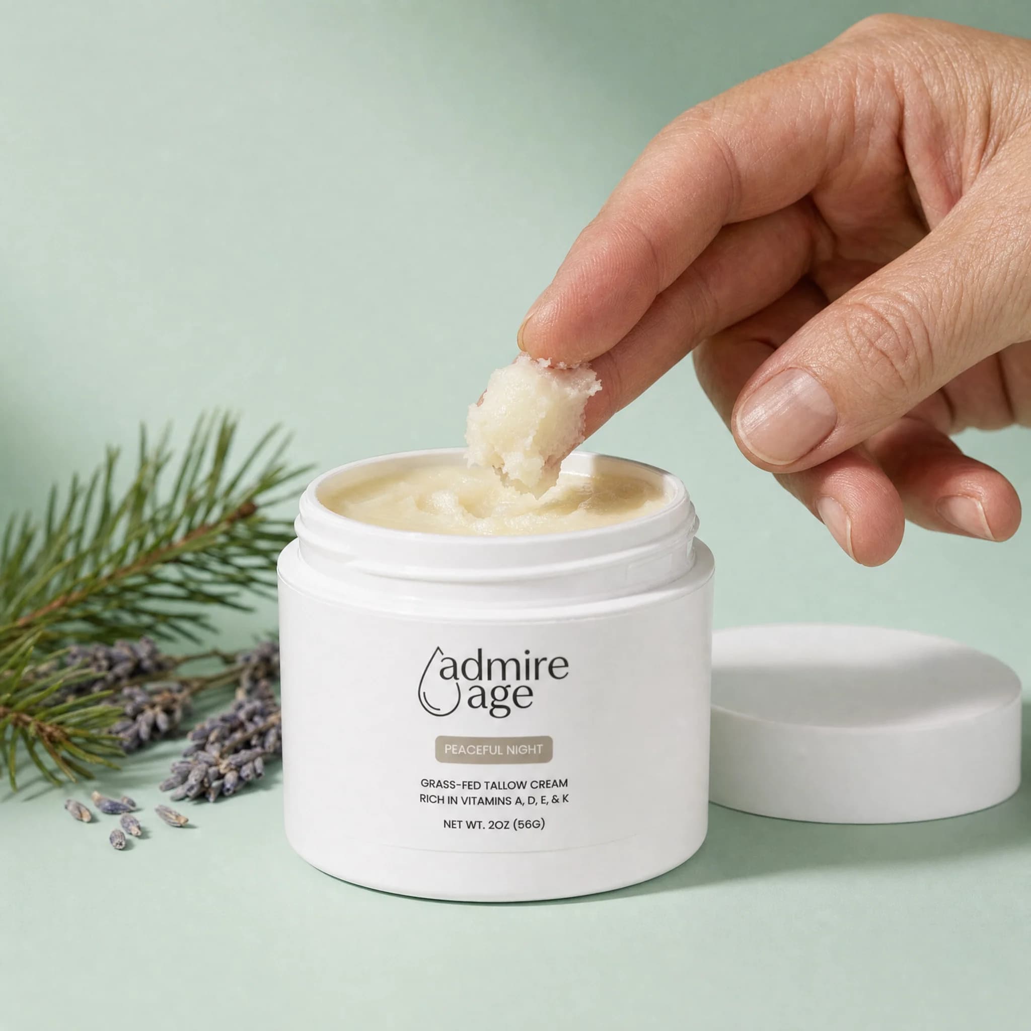 A hand lifting a small dollop of Peaceful Night tallow balm from the open jar